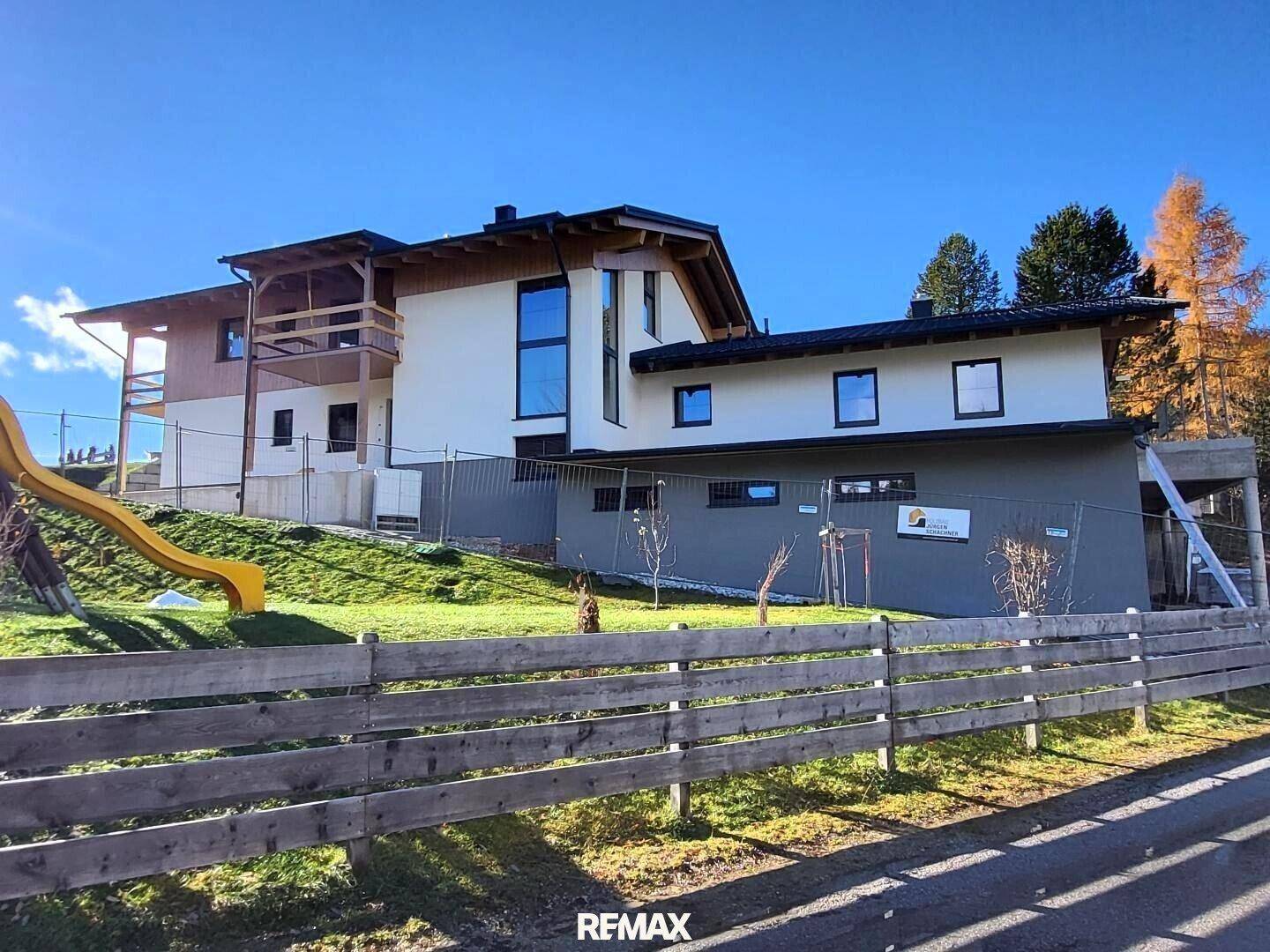 Modernes Einfamilienhaus mit großzügigem Gartenbereich, Rutsche und Holzzaun unter blauem Himmel.
