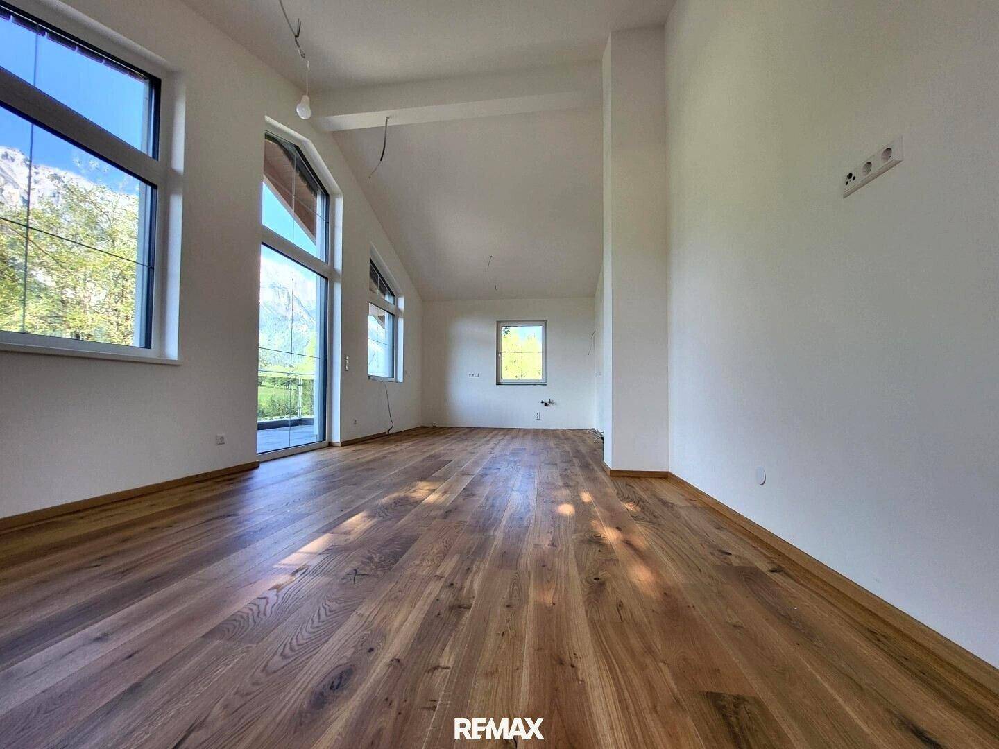 Lichtdurchfluteter Wohnraum mit Holzboden, hohen Decken und weitem Blick ins Grüne.
