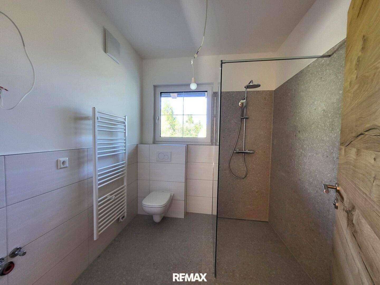 Modernes Badezimmer mit ebenerdiger Dusche, WC und beheiztem Handtuchhalter.