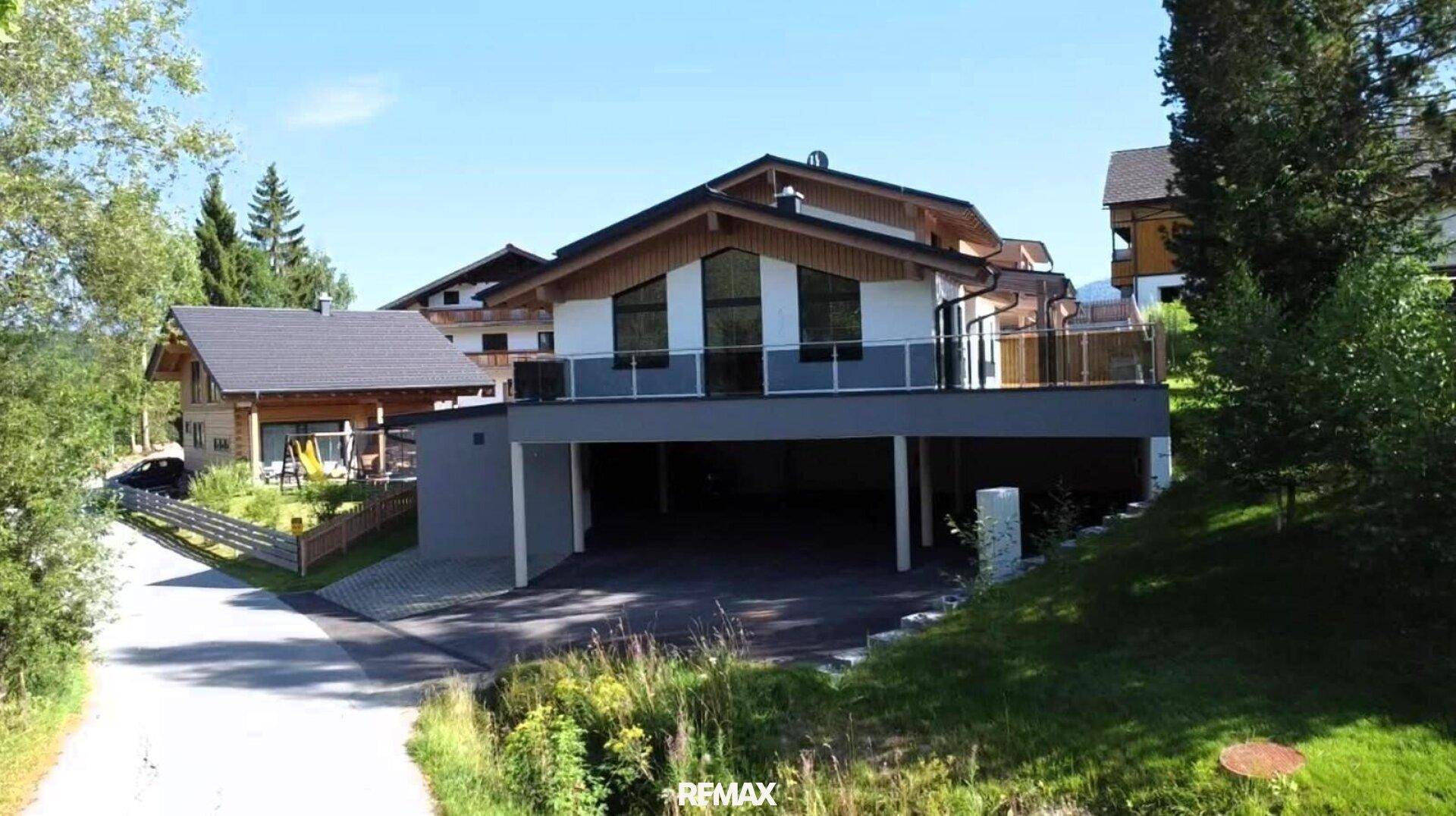 Modernes Wohnhaus mit großzügiger Terrasse und integriertem Carport in alpiner Umgebung.