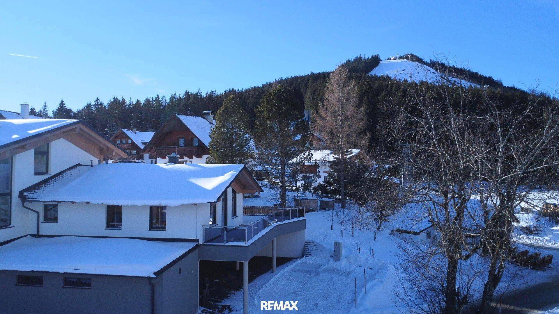 Winterliche Ansicht des Hauses mit verschneiter Umgebung und Blick auf einen bewaldeten Hügel.