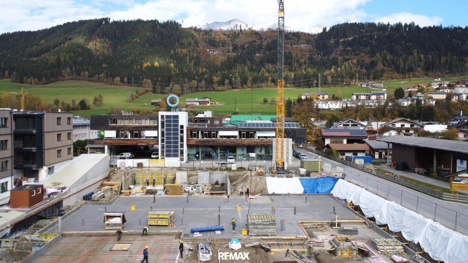 Baustelle mit Fundamentarbeiten und einem Kran, umgeben von grünen Hügeln und Bergen.
