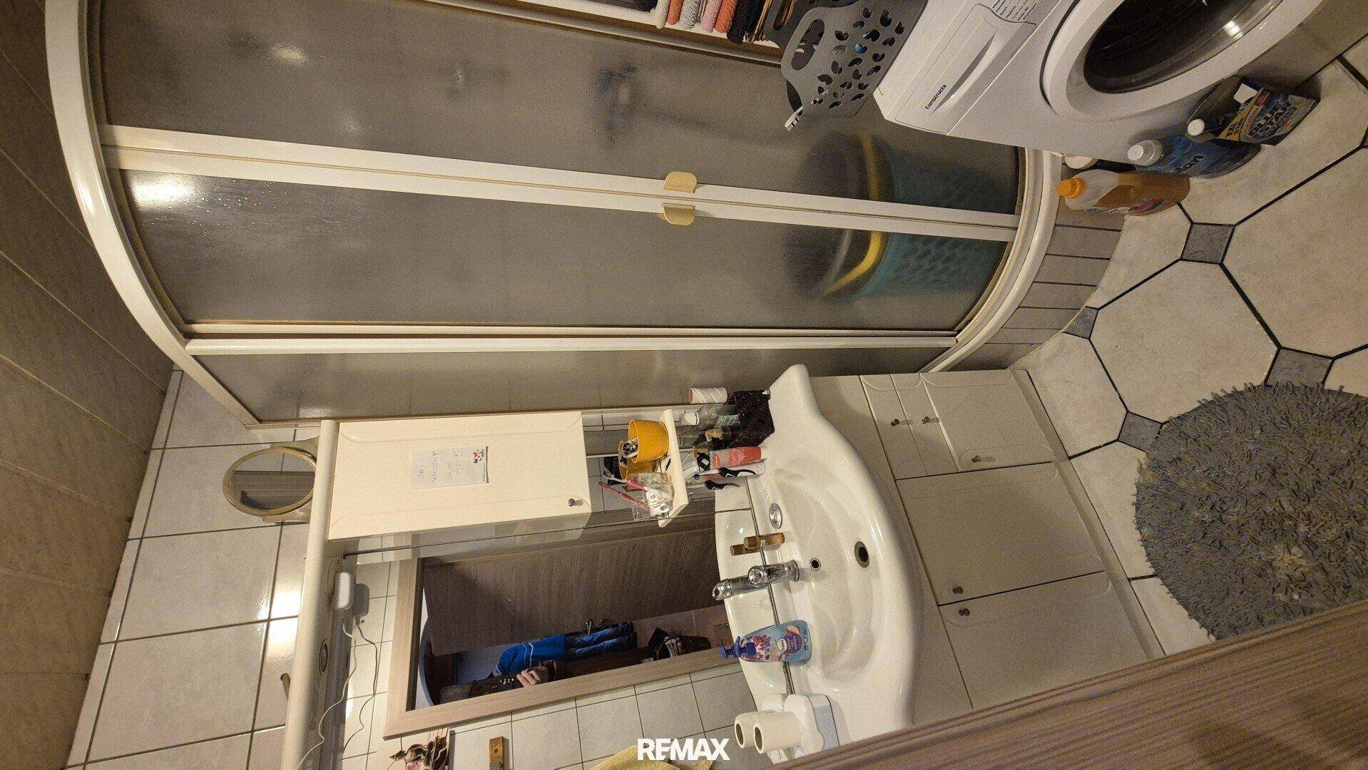 Funktionales Badezimmer mit Duschkabine, Waschbecken und Fliesenboden.