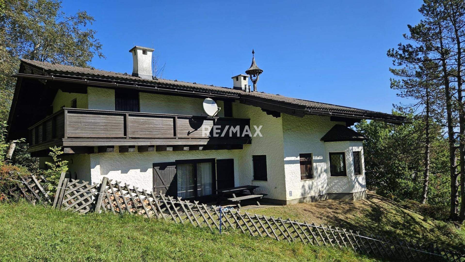 Traditionelles Haus mit Holzbalkon und kleiner Terrasse, eingebettet in eine grüne Hügellandschaft.