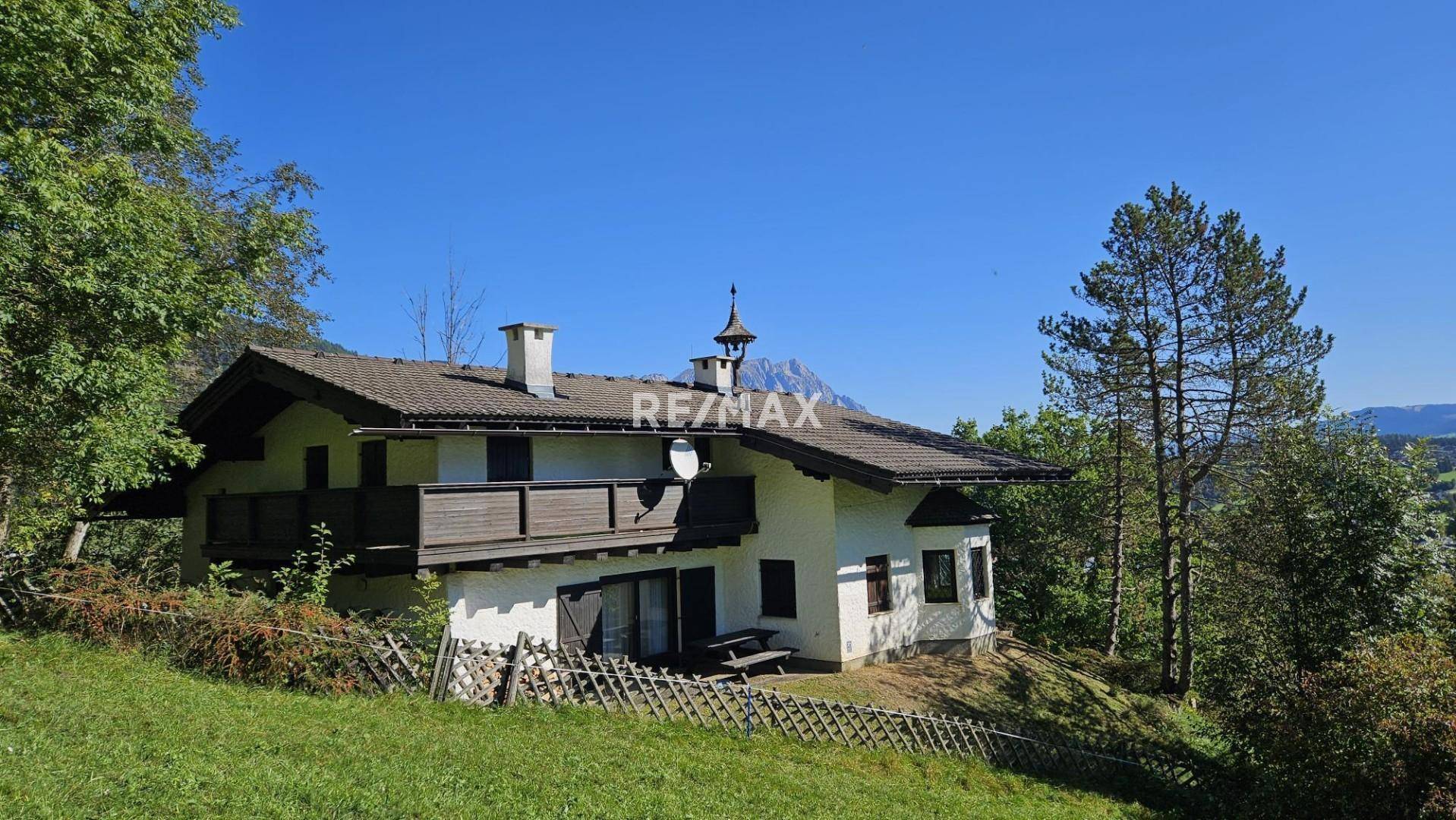 Traditionelles Haus mit Holzbalkon und Terrasse, umgeben von grüner Natur und Bäumen.