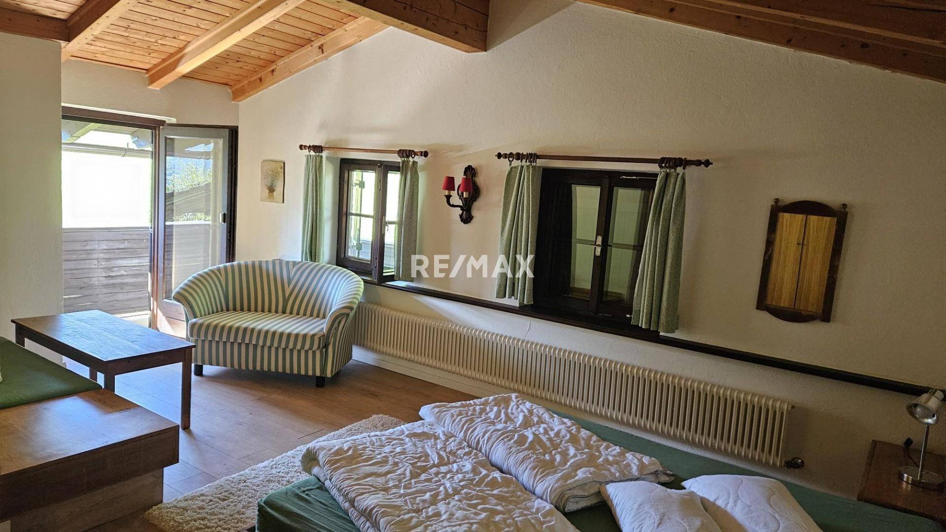 Gemütliches Schlafzimmer mit Holzbalkendecke, Parkettboden und Zugang zum Balkon.