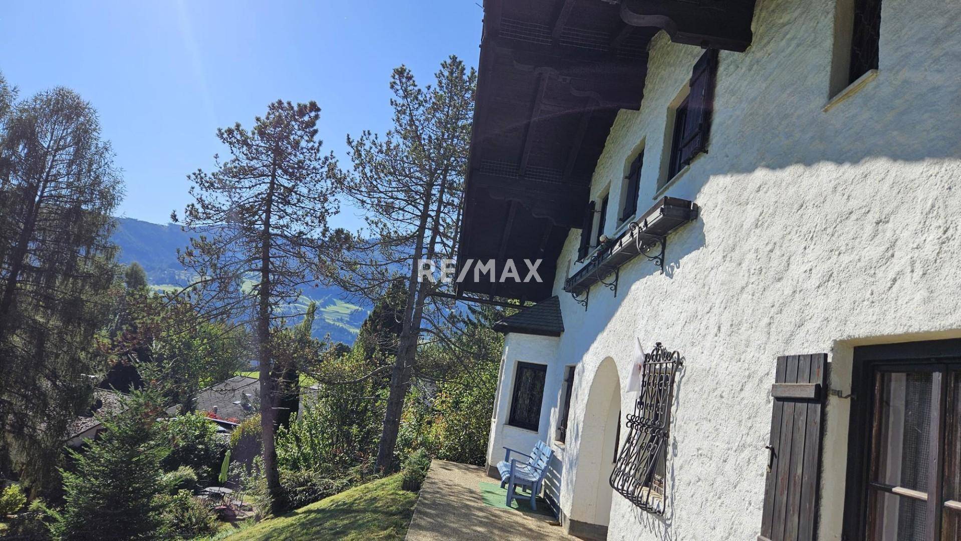 Seitenansicht des Hauses mit rustikalen Fenstern und Blick auf die umliegende Hügellandschaft.