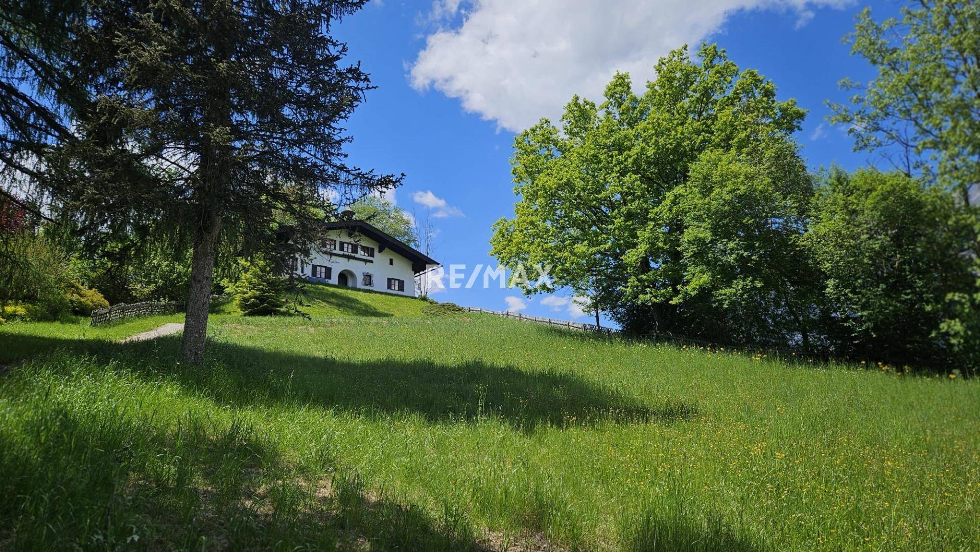 Charmantes Haus auf einer Anhöhe, umgeben von weitläufigen grünen Wiesen und Bäumen.