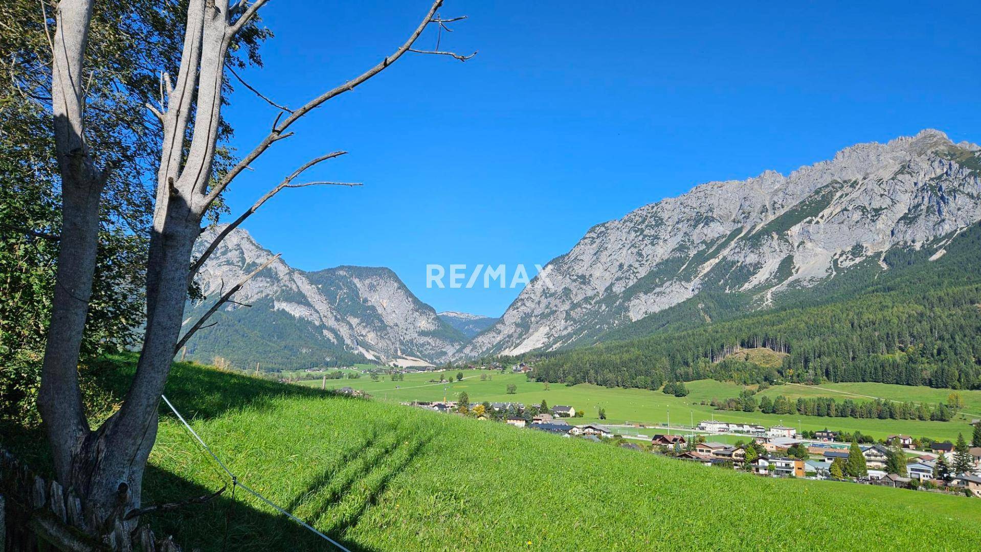 Weitläufige Landschaft mit majestätischen Bergen, grünen Wiesen und einem Dorf in der Ferne.