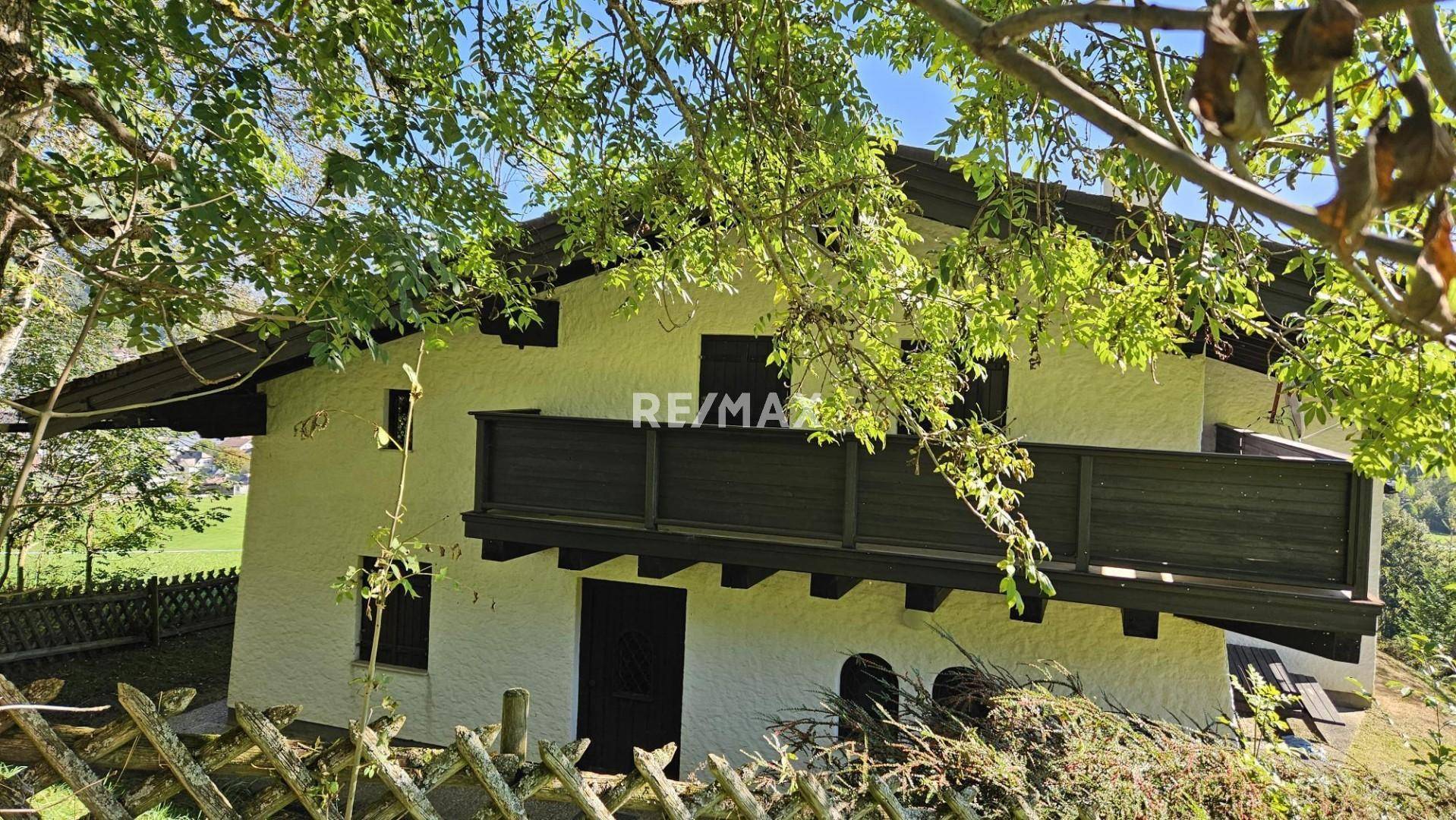 Nahaufnahme des Hauses mit Holzbalkon und rustikalen Fensterläden, umgeben von Bäumen.