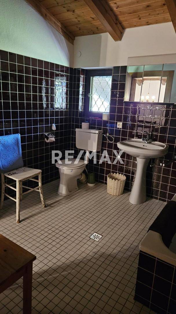 Badezimmer mit dunklen Fliesen, WC, Waschbecken und einem kleinen Fenster.