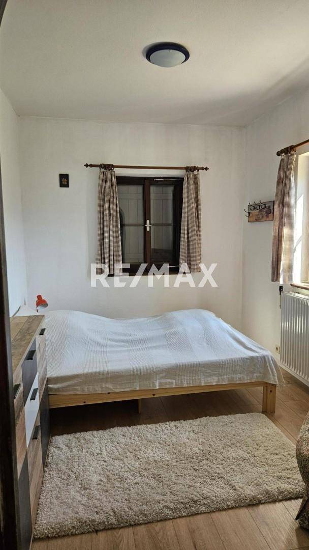 Helles Schlafzimmer mit Holzbett, Teppich und Fenster, das viel Tageslicht hereinlässt.