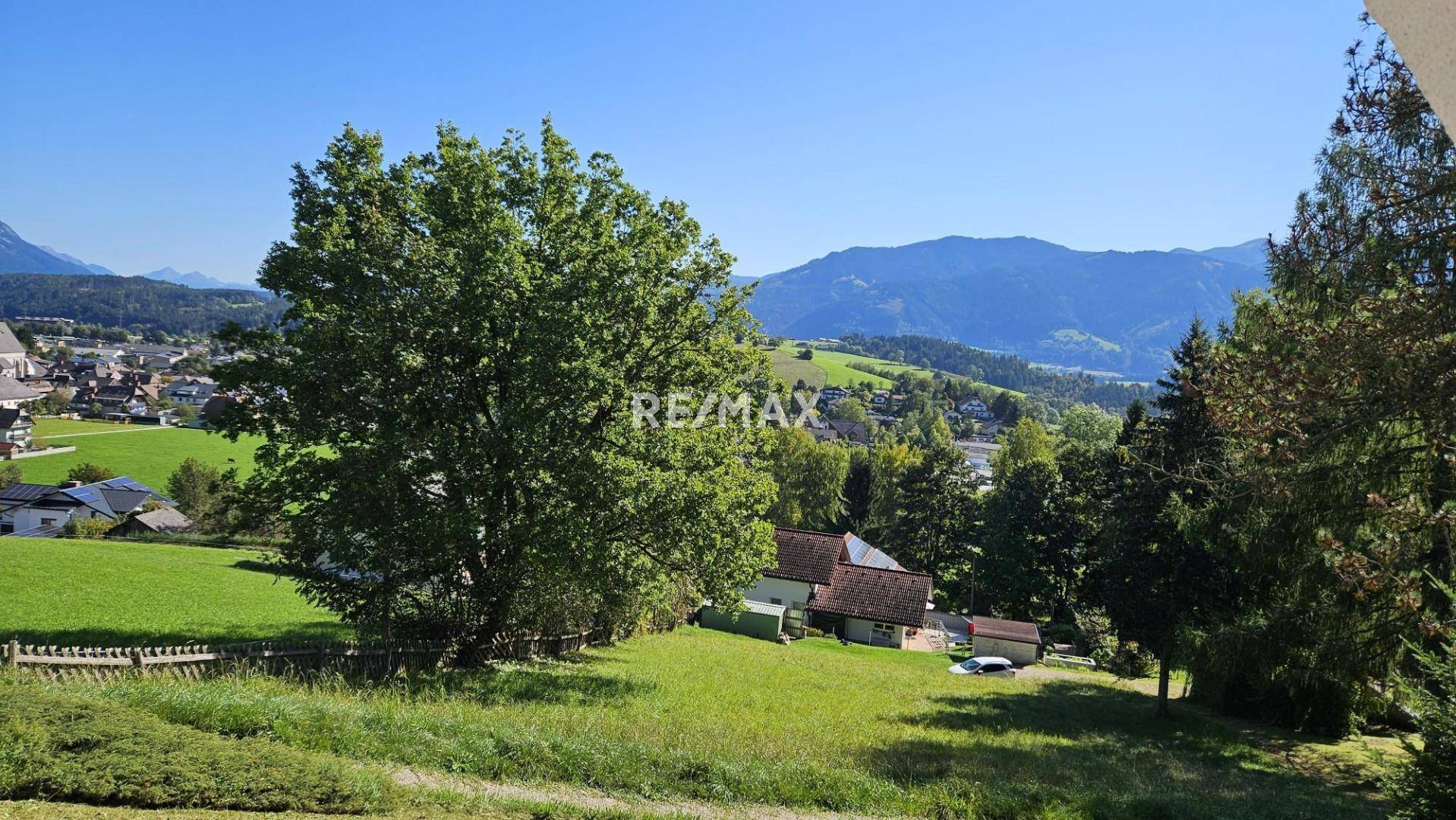 Weitläufiger Blick auf grüne Wiesen, Bäume und die umliegende Berglandschaft.