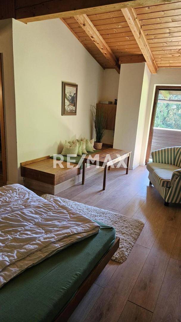 Helles Schlafzimmer mit Holzbalkendecke, Holzboden und einer gemütlichen Sitzecke.