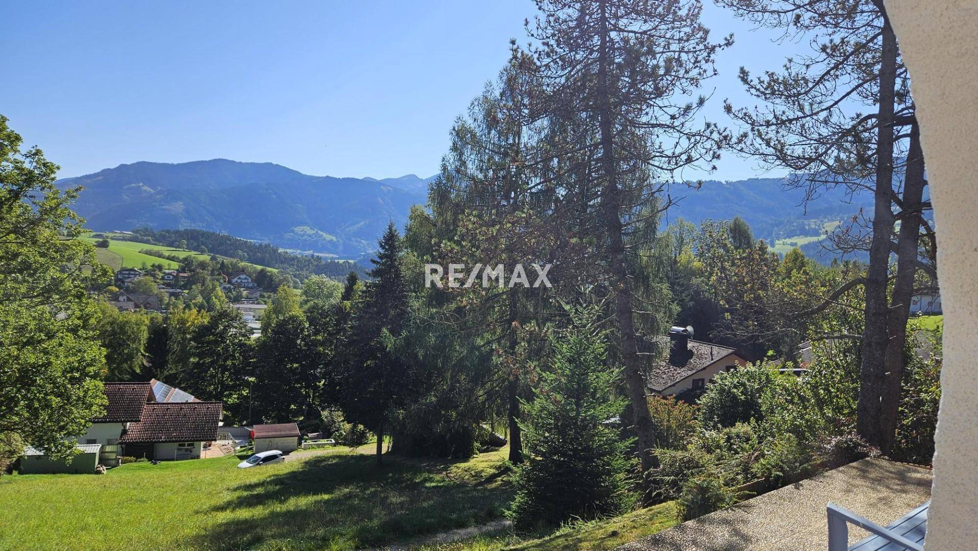 Panoramablick auf die umliegende Hügellandschaft und das Tal mit vereinzelten Häusern.