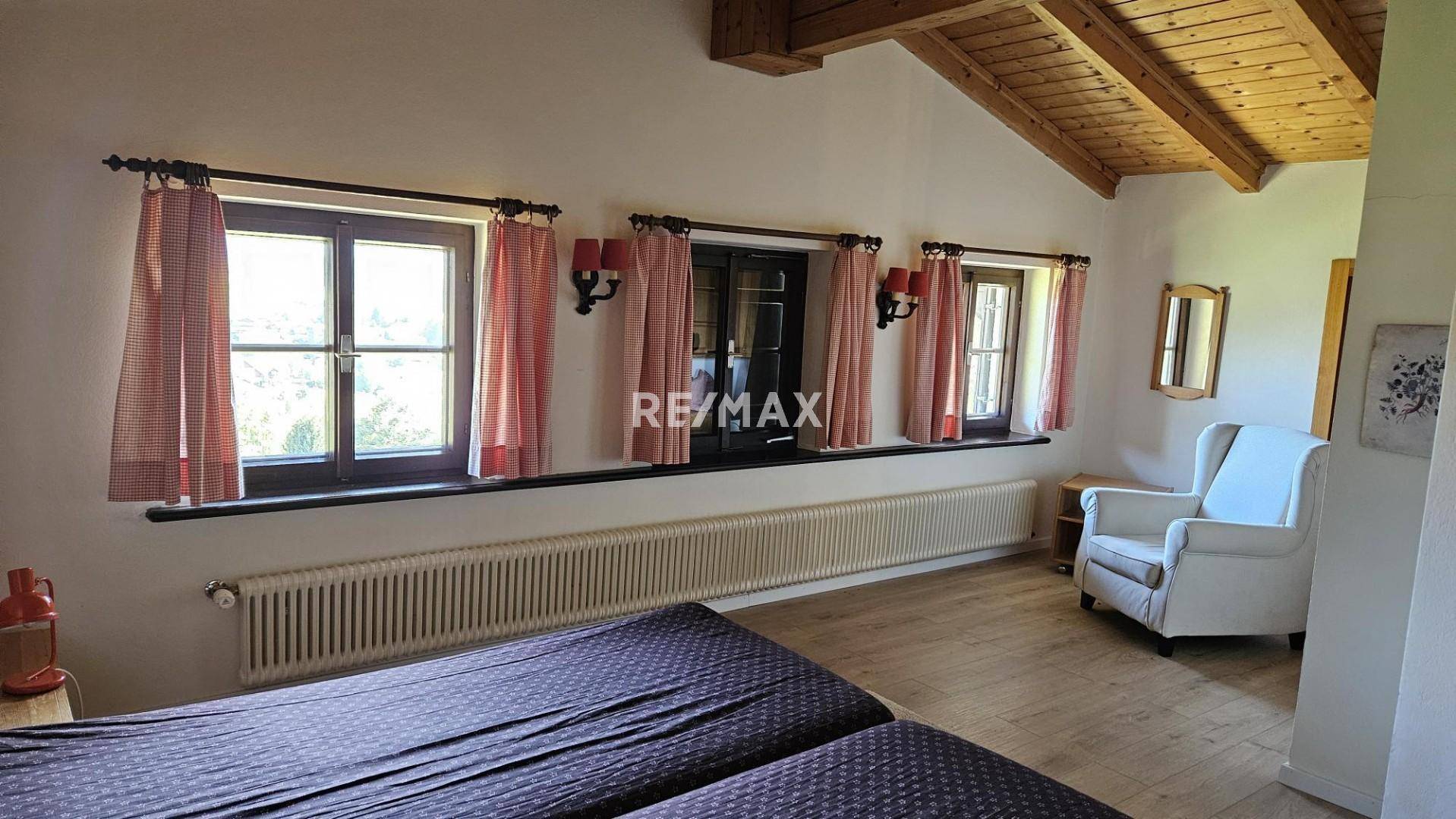 Helles Schlafzimmer mit Holzbalkendecke, Parkettboden und mehreren Fenstern.