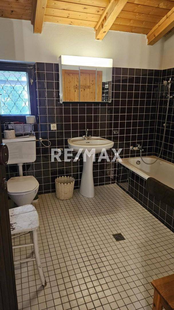 Badezimmer mit dunklen Fliesen, Badewanne, Waschbecken und Spiegelschrank.