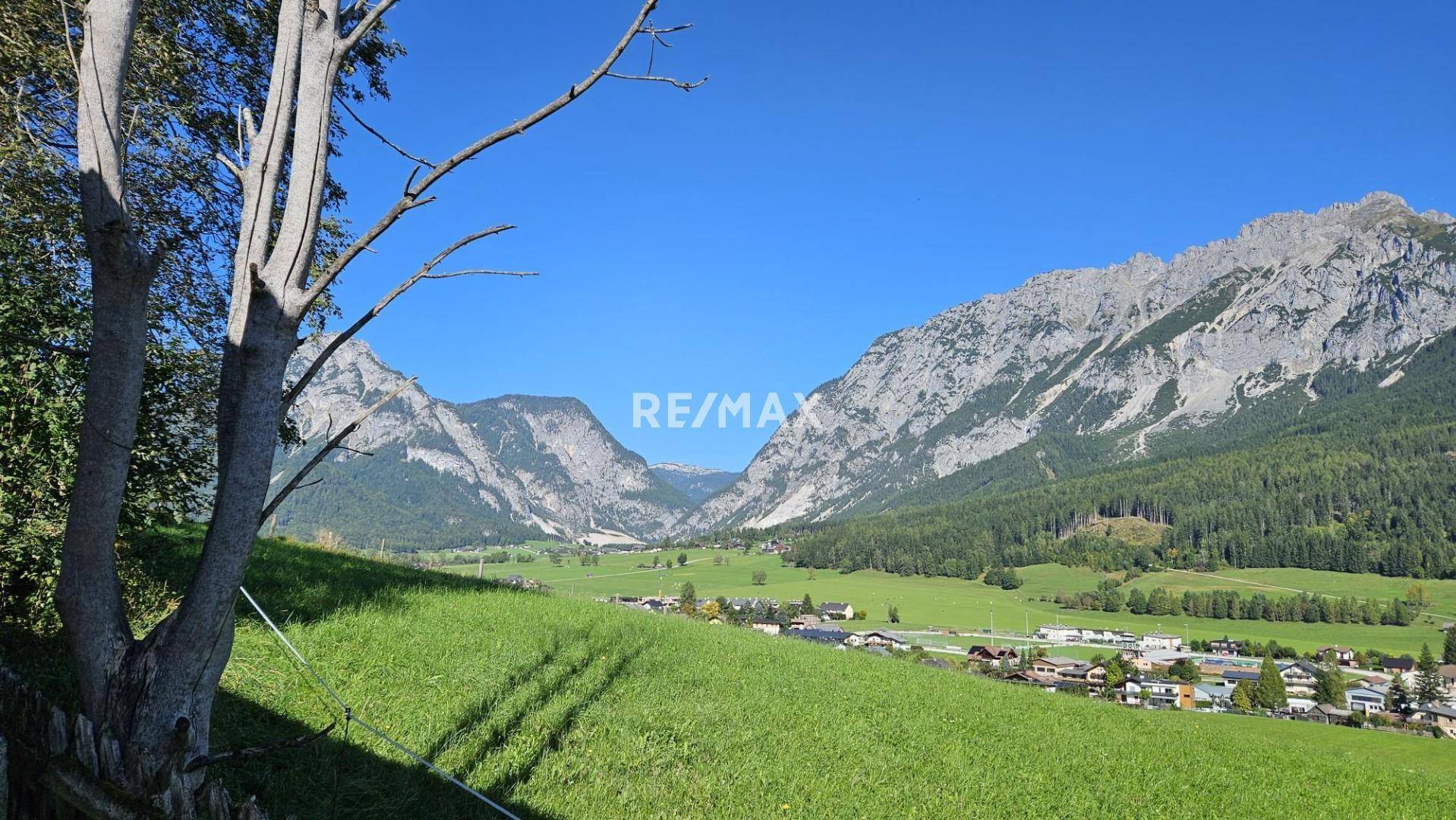 Malerische Berglandschaft mit weiten grünen Wiesen und einem kleinen Dorf in der Ferne.