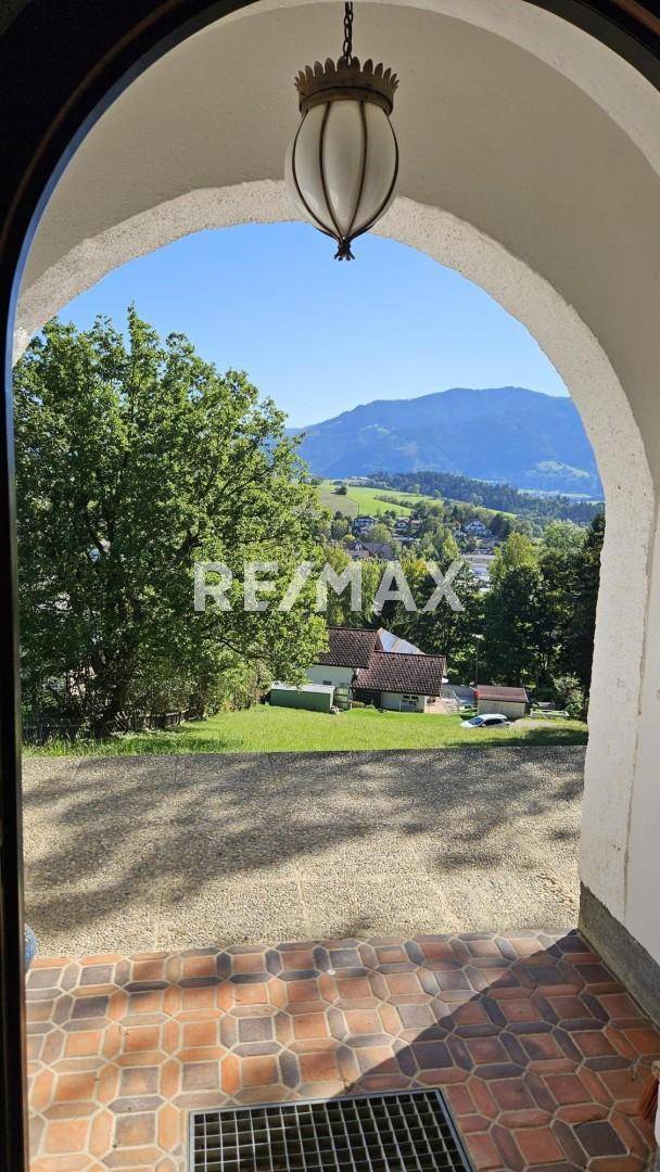 Blick durch einen Torbogen auf die grüne Hügellandschaft und das sonnige Tal.