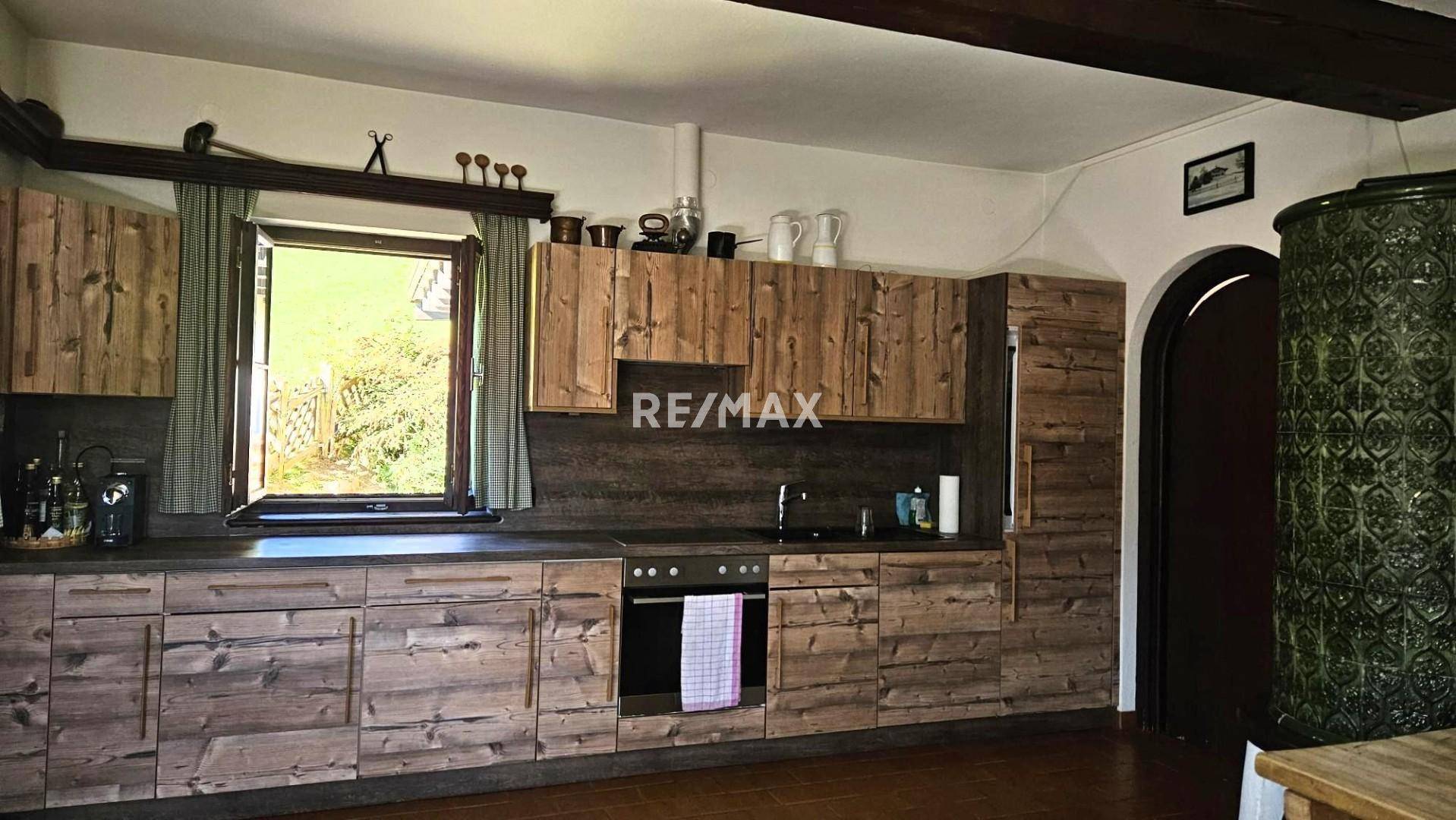 Geräumige Küche mit Holzschränken, Kachelofen und Fenster mit Blick ins Grüne.