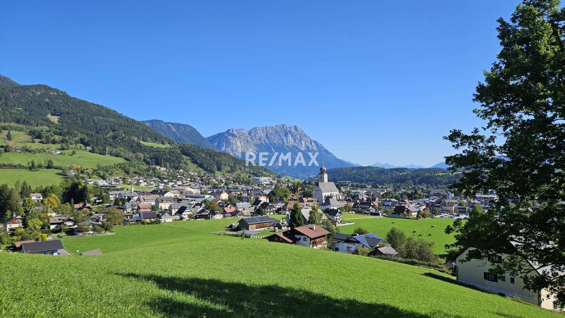 Panoramablick auf ein malerisches Dorf in einem Tal, umgeben von grünen Hügeln und Bergen.
