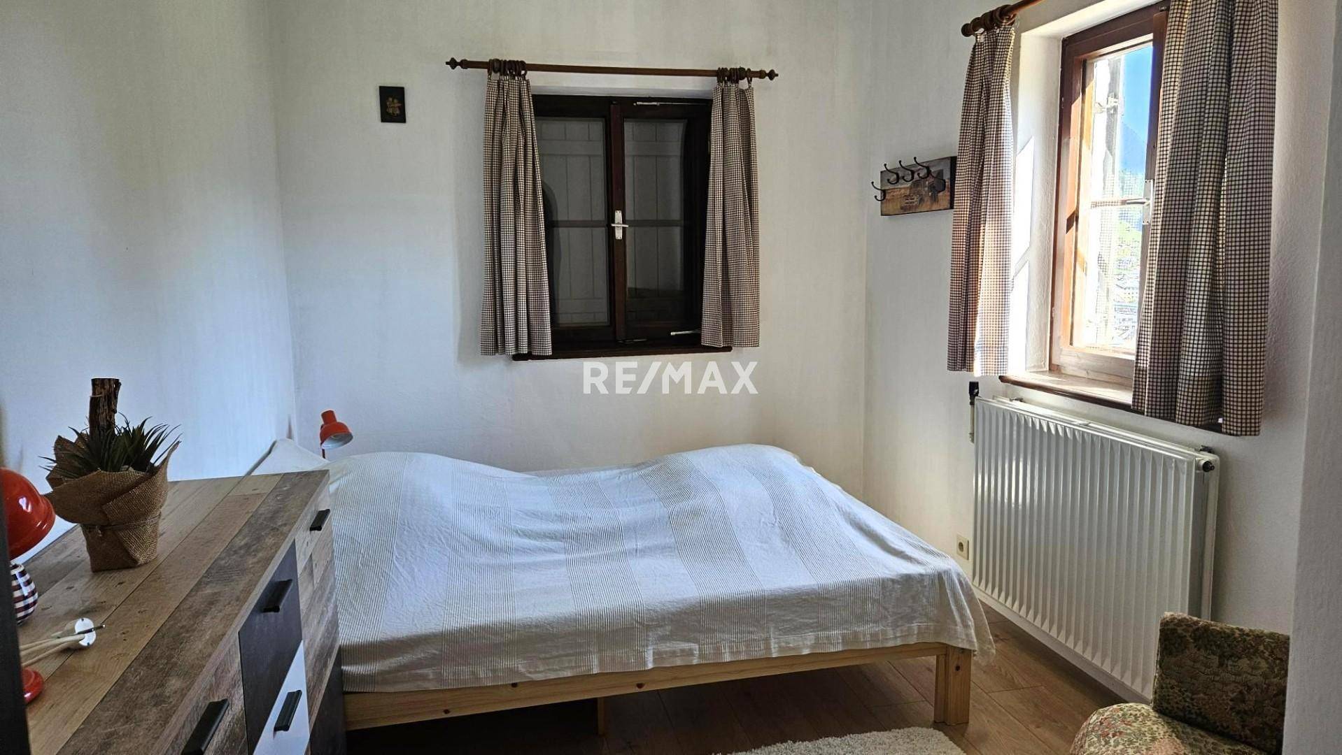 Einfaches Schlafzimmer mit Holzbett, Parkettboden und Fenster mit Blick ins Grüne.