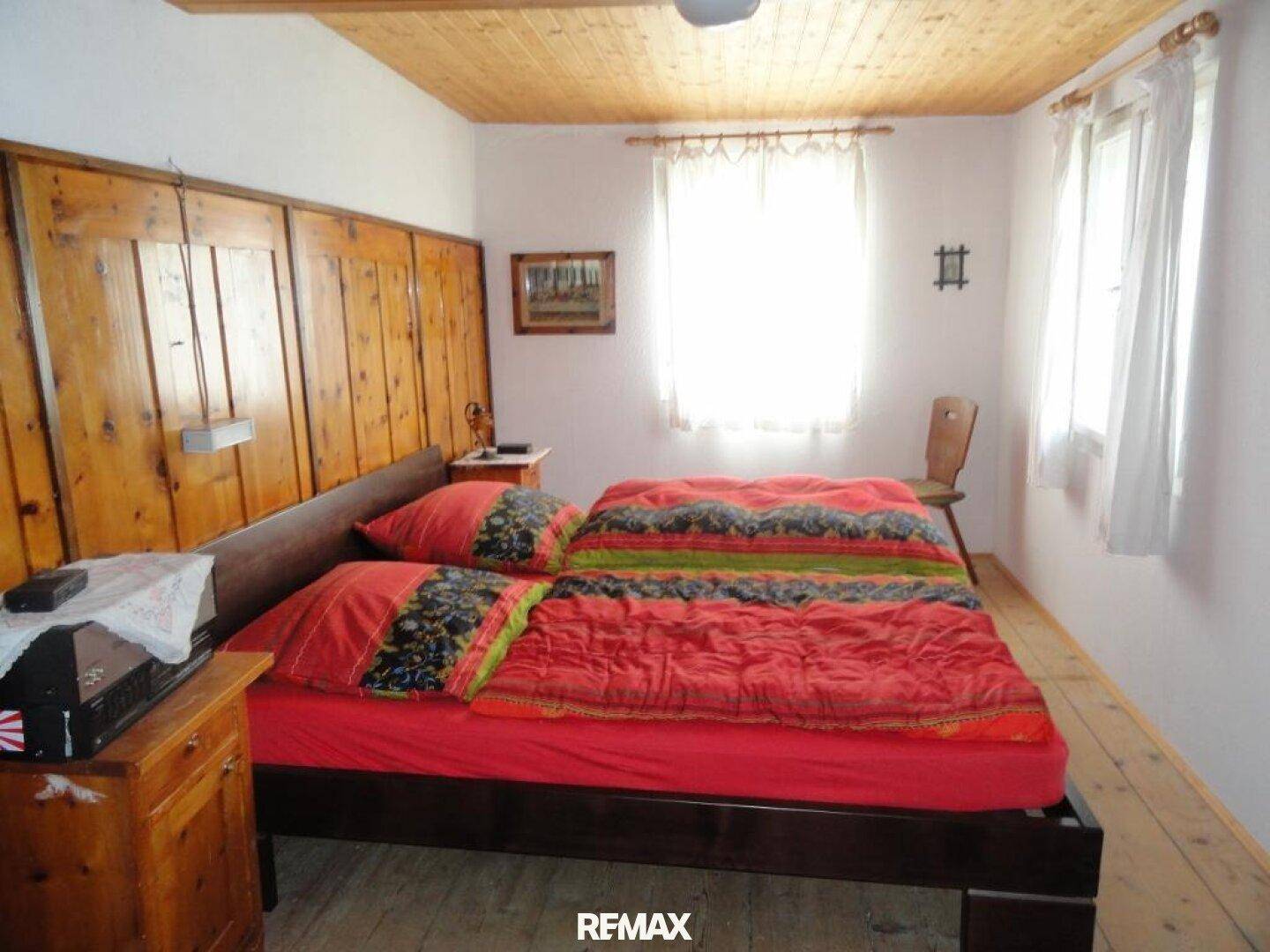 Gemütliches Schlafzimmer mit Holzbalkendecke, Holzvertäfelung und hellen Fenstern.
