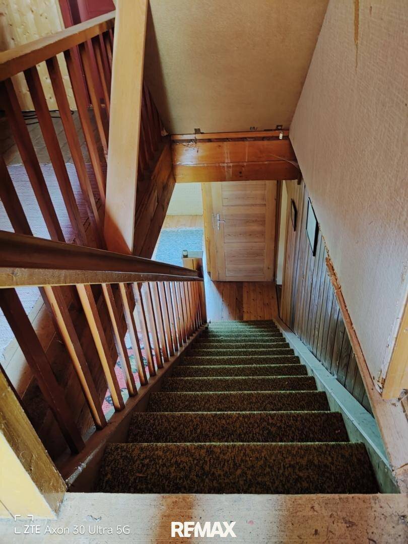 Holztreppe mit Teppichstufen und Holzgeländer, die in ein Obergeschoss führt.