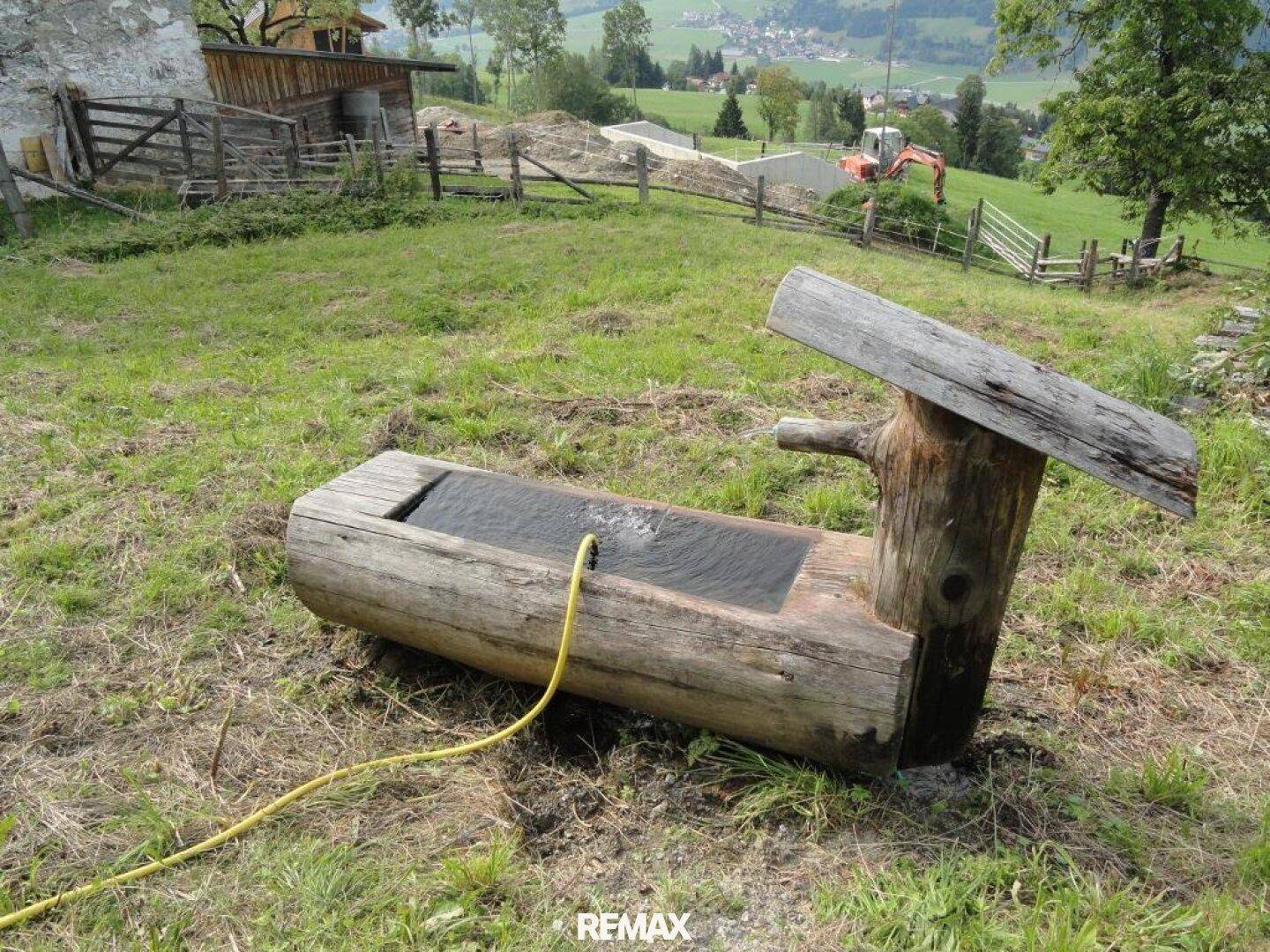 Rustikaler Holzbrunnen mit fließendem Wasser in einem grünen Gartenbereich.
