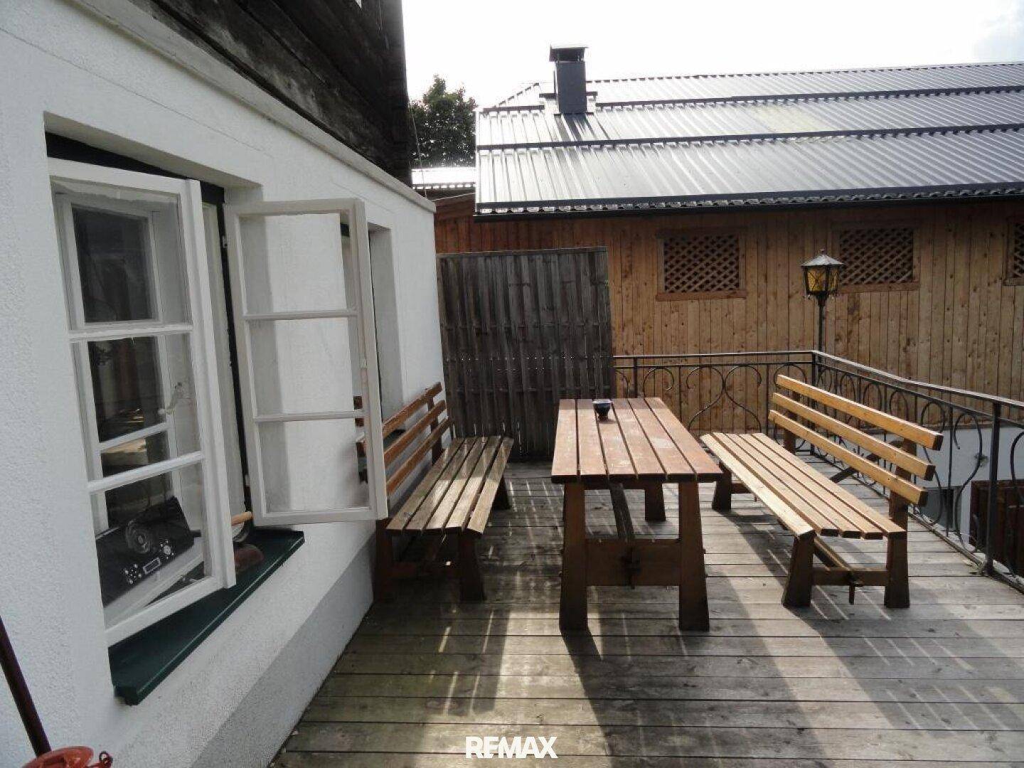 Rustikale Holzterrasse mit Sitzgelegenheiten und Blick auf ein Nebengebäude.