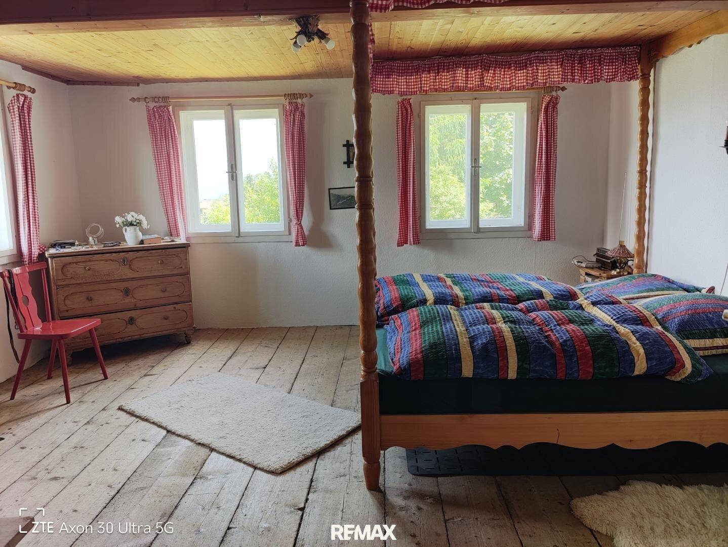 Geräumiges Schlafzimmer im Landhausstil mit Holzboden, Himmelbett und karierten Vorhängen.