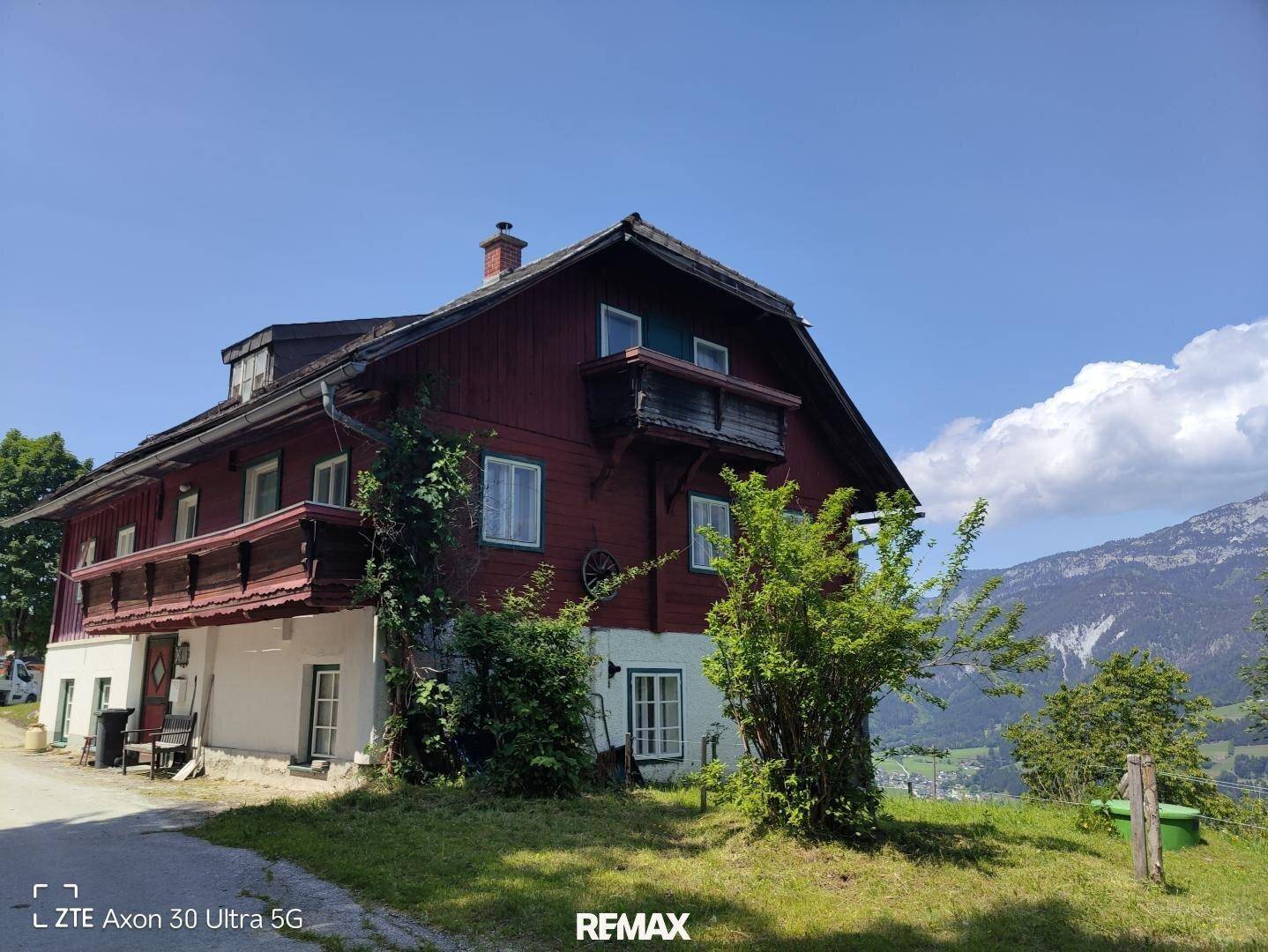 Traditionelles Holzhaus mit roten Fassaden und Balkonen in alpiner Umgebung.