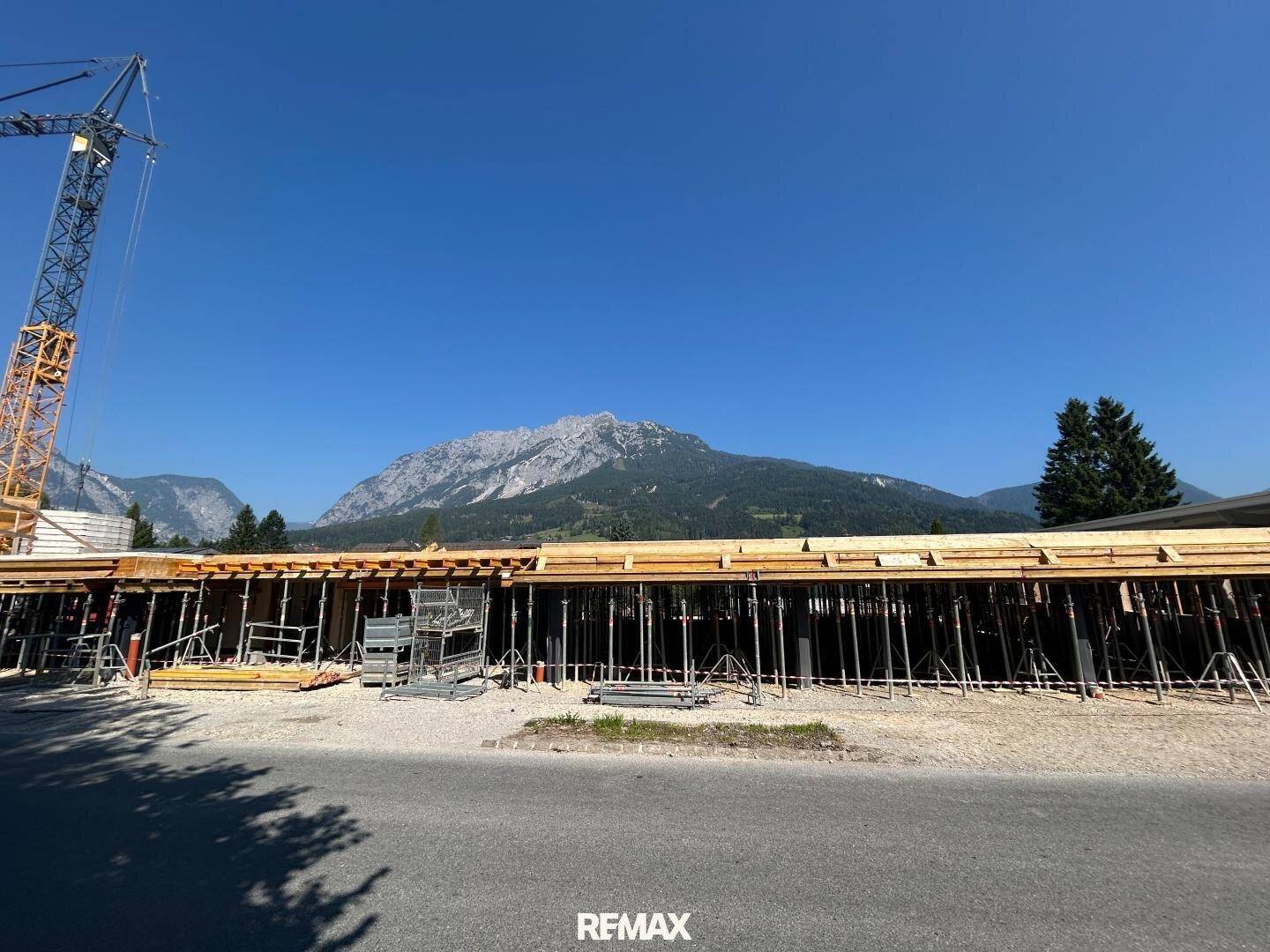Baustelle mit Schalung und Stützen für ein neues Gebäude vor beeindruckender Berglandschaft.