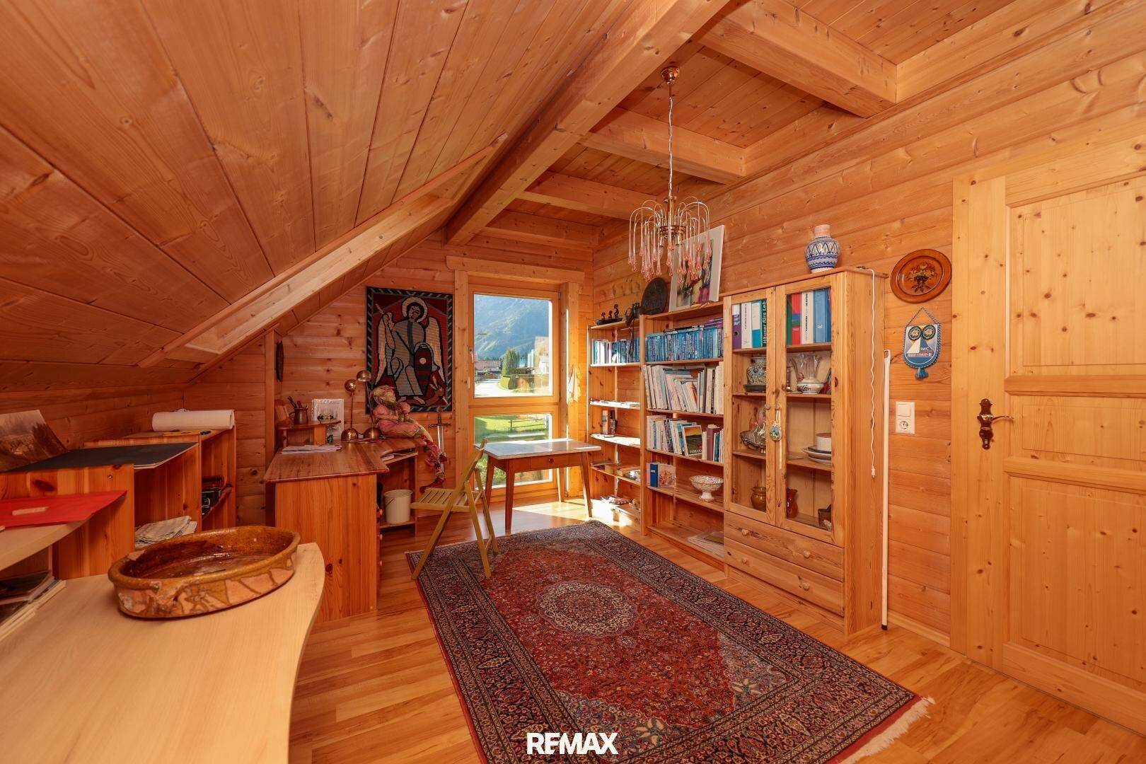 Helles Arbeitszimmer mit Holzwänden, Bücherregalen und Bergblick durch das Fenster.