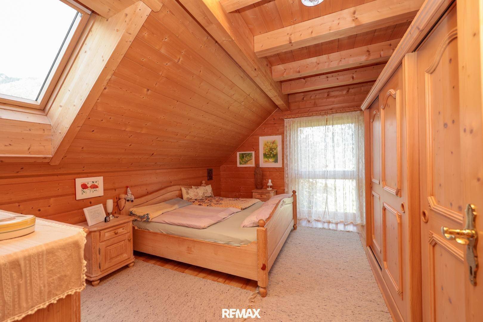 Gemütliches Schlafzimmer im Dachgeschoss mit Holzwänden, Dachfenster und Teppichboden.