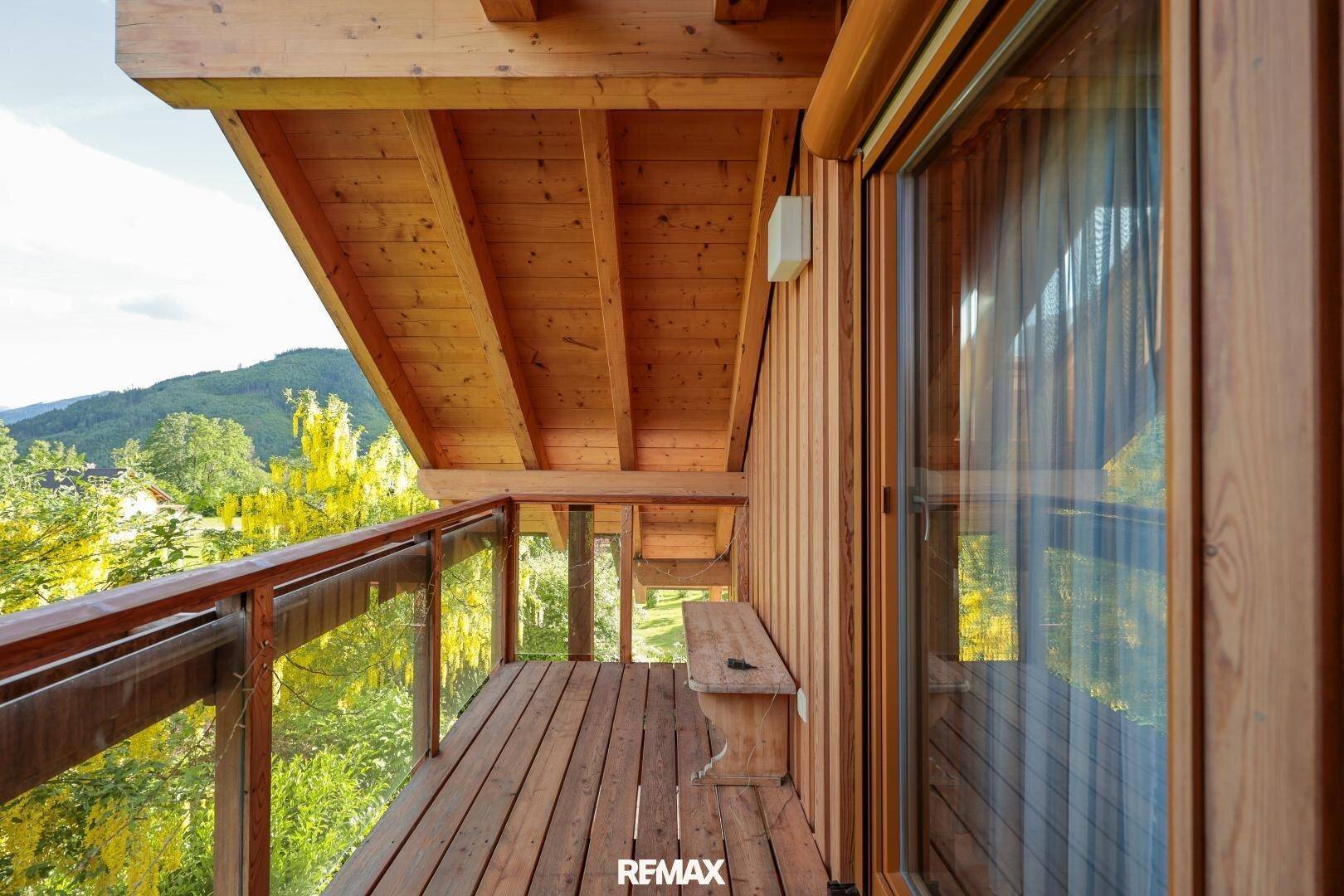 Holzverkleideter Balkon mit Glasgeländer und Blick auf die grüne Umgebung.