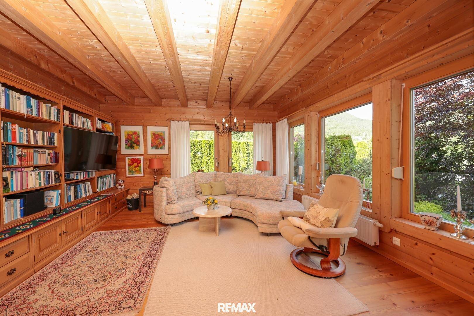 Gemütliches Wohnzimmer mit Holzbalkendecke, großem Bücherregal und weitem Ausblick.