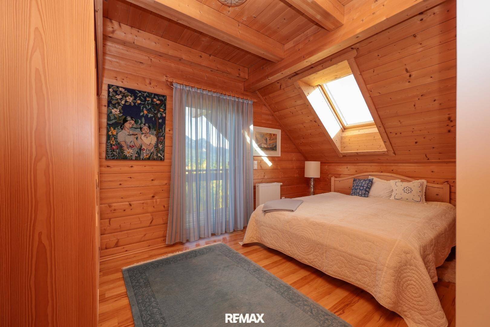 Schlafzimmer im Dachgeschoss mit Holzwänden, Dachfenster und Blick ins Grüne.