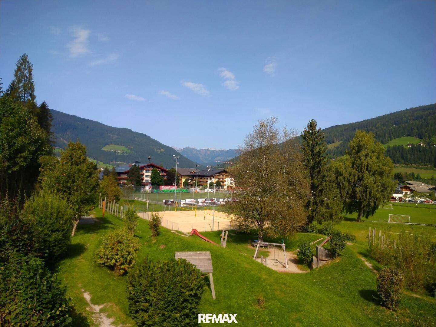 Malerischer Blick auf die Berge und ein Tal, mit einem Spielplatz und Sportfeldern im Vordergrund.