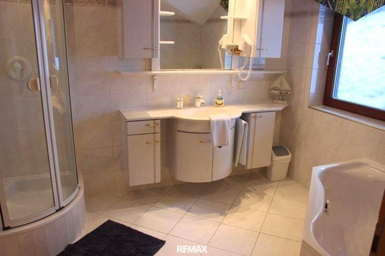 Funktionales Badezimmer mit Duschkabine, Waschtisch und Fenster, hell gefliest in weißem Design.