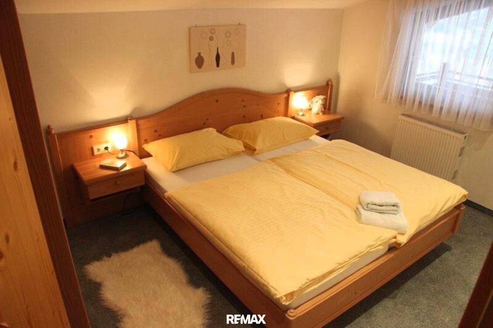 Komfortables Schlafzimmer mit Doppelbett und grünem Teppichboden, mit traditionellen Holzmöbeln.