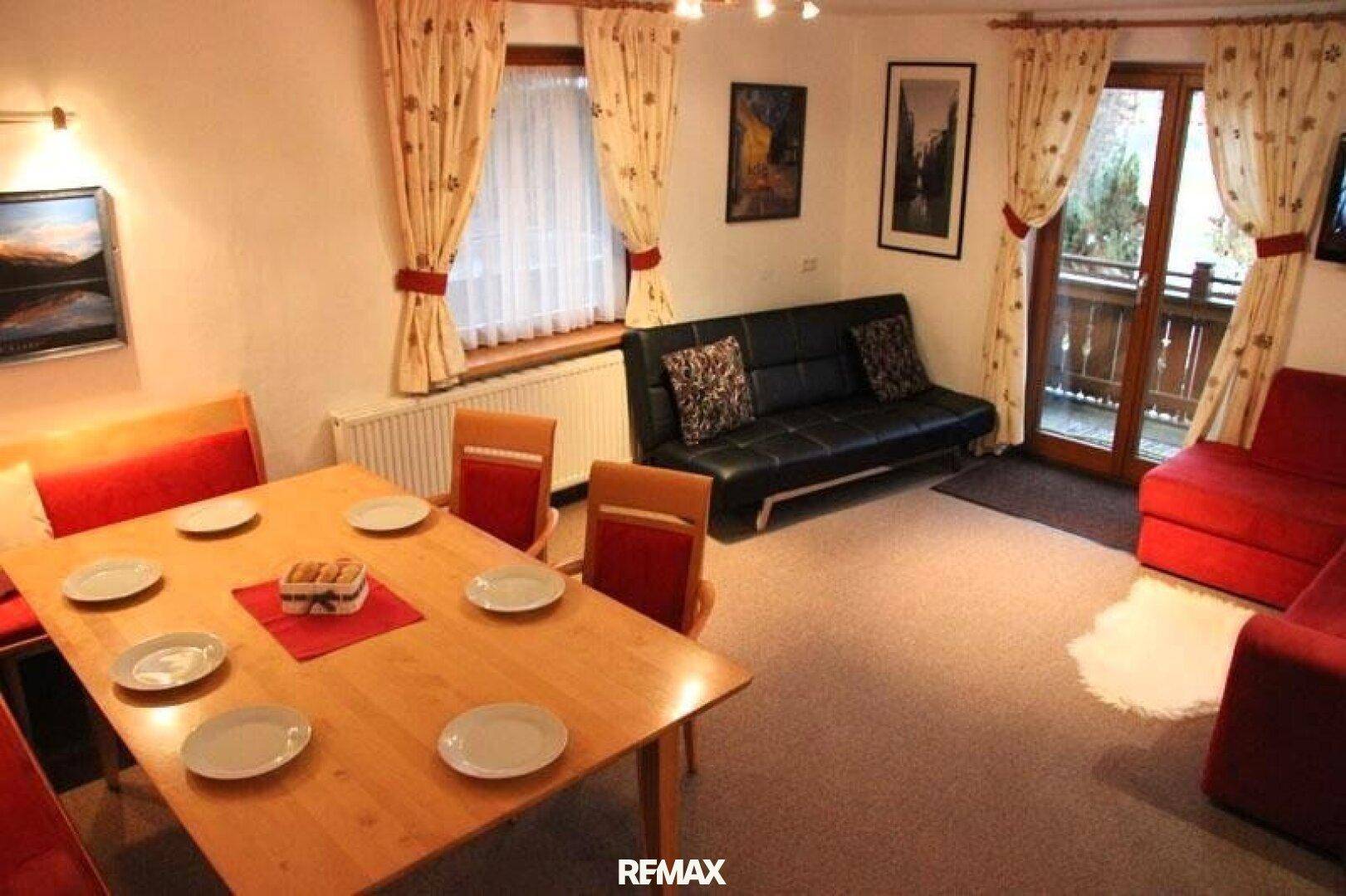 Einladender Wohn-Essbereich mit gedecktem Esstisch, bequemen Sofas und Zugang zum Außenbereich.