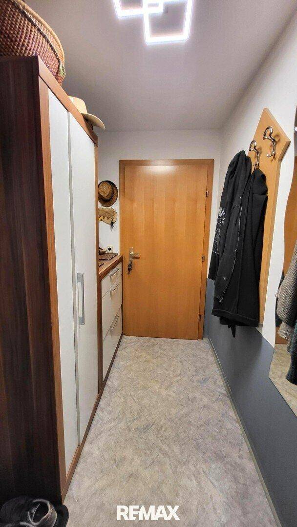 Schmaler Flur mit Holztür, Garderobe und praktischem Stauraum.
