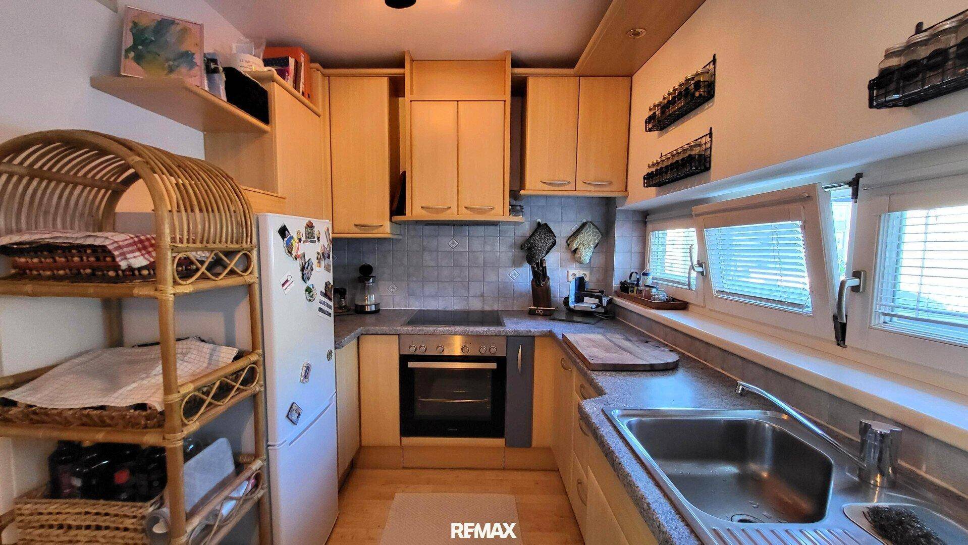 Funktionale Einbauküche mit hellen Holzschränken, Geräten und Fenster.