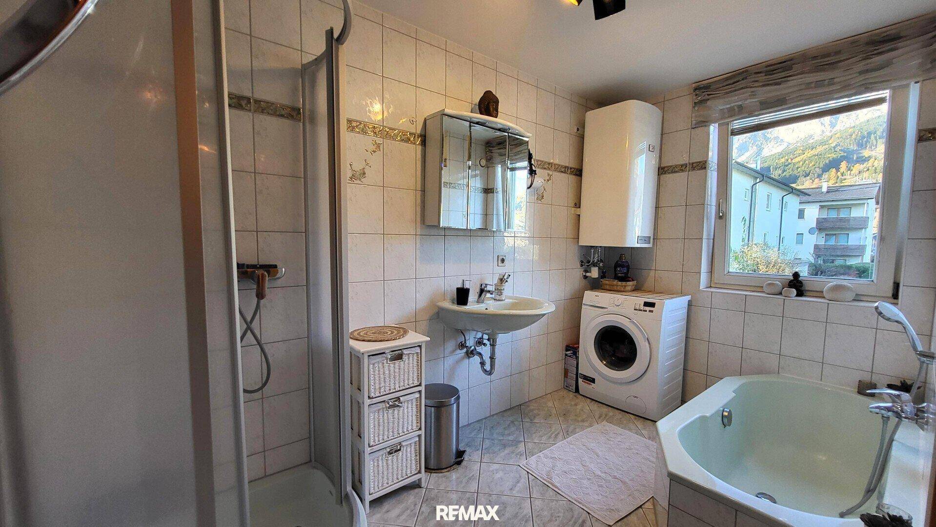 Gefliestes Badezimmer mit Dusche, Badewanne, Waschmaschine und Fenster.
