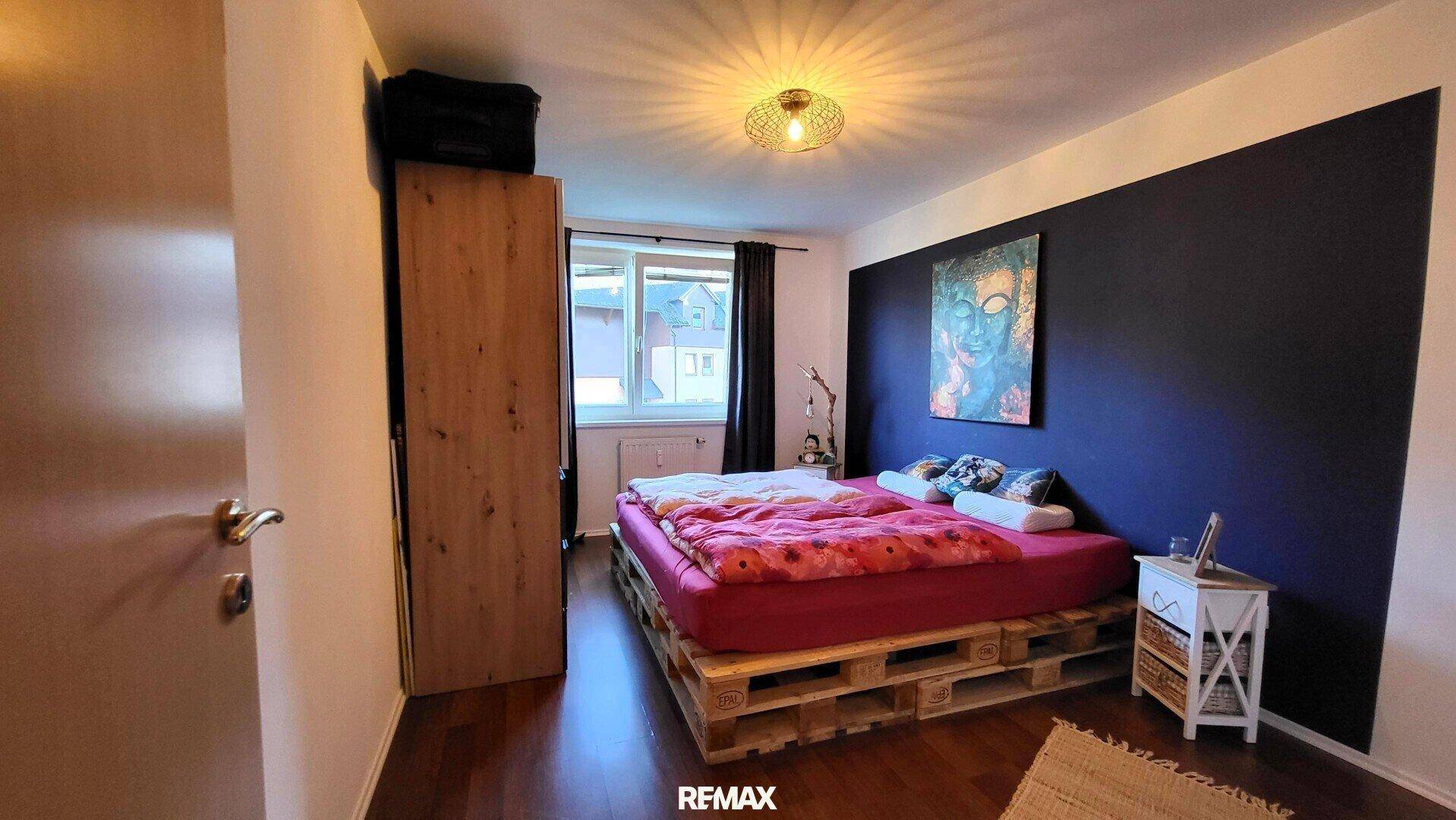 Schlafzimmer mit Palettenbett, großem Kleiderschrank und blauer Akzentwand.