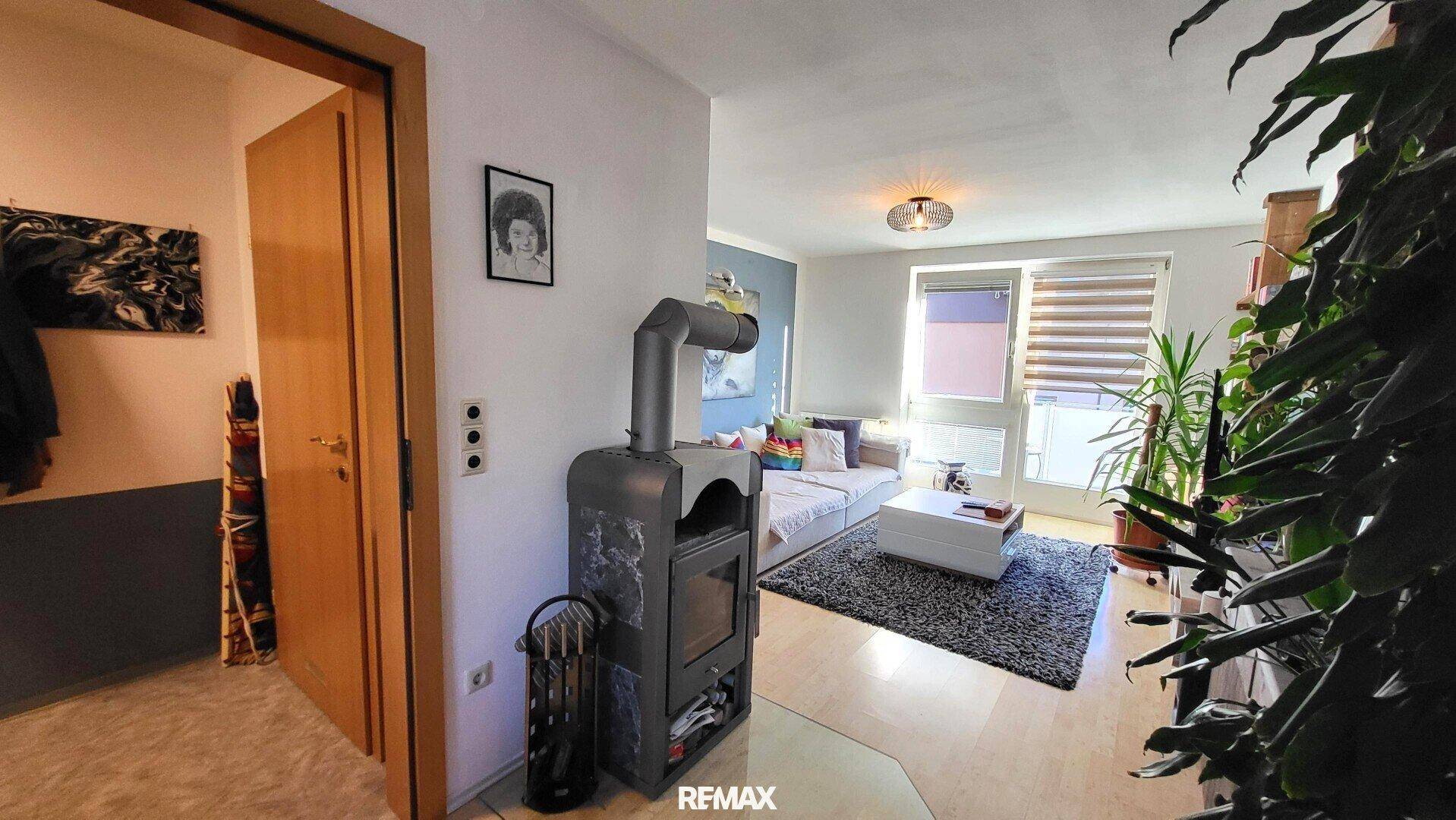 Gemütliches Wohnzimmer mit Kaminofen, Sofa und großem Fenster.