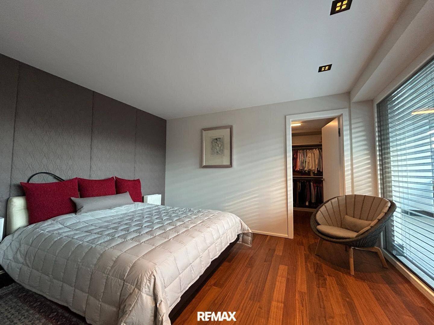 Geräumiges Schlafzimmer mit großem Bett, Sitzgelegenheit und Zugang zum Ankleidezimmer.