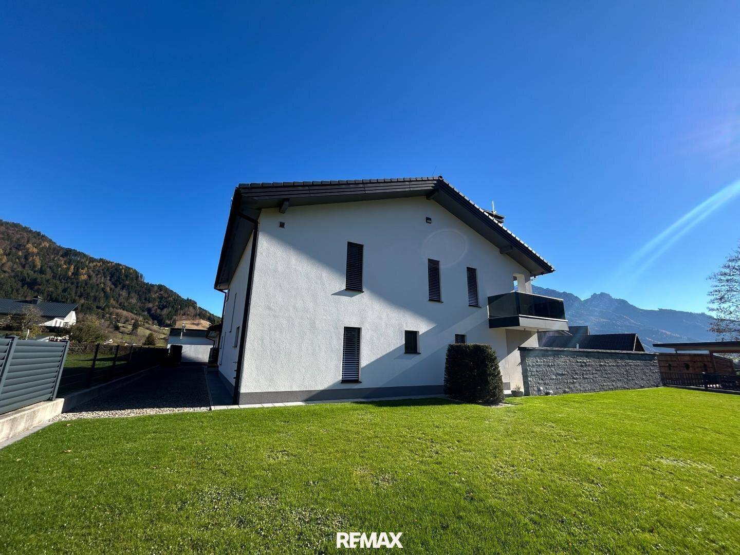 Seitliche Ansicht eines modernen Hauses mit weißer Fassade, Rasenfläche und Bergblick.