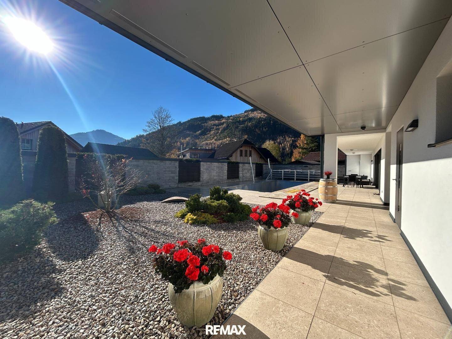Sonnige Terrasse mit Fliesenboden, Blick auf den Garten und die umliegende Berglandschaft.
